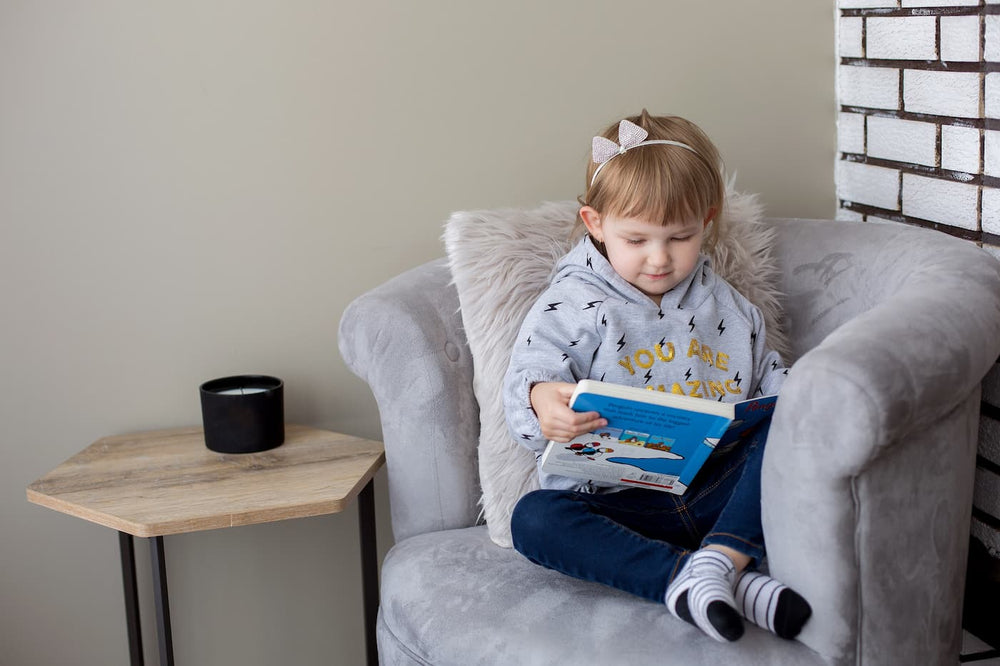 Child reading a book in a cozy armchair with a side table and decorative elements.